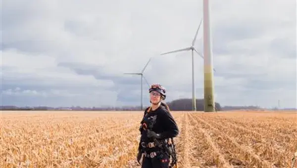 Technicienne éolien Boralex dans un champ face à une éolienne au Canada