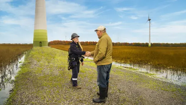 Poignée de main entre une technicienne éolienne et un homme face à une éolienne