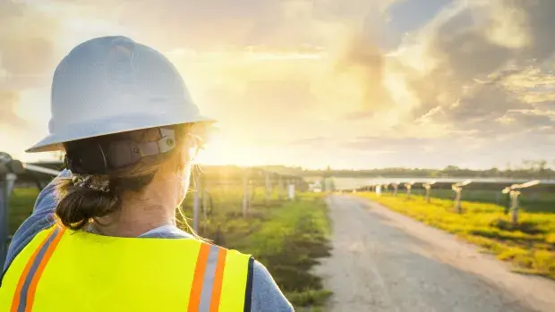Technicienne faisant face à des panneaux solaires et un couché de soleil