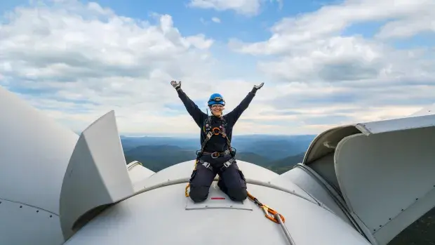 Technicienne souriante sur le toit d'une éolienne levant les mains au ciel