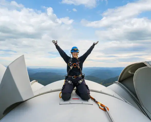 Technicienne souriante sur le toit d'une éolienne levant les mains au ciel